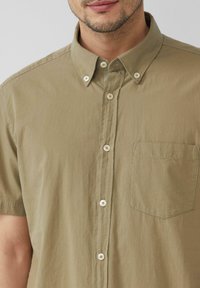 Kurzärmliges olivgrünes Hemd aus leichtem Stoff, mit einem Button-Down-Kragen, fünf Knöpfen und einer Brusttasche.