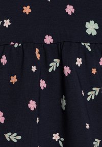 Námorná tkanina s kvetinovým vzorom, ktorá obsahuje ružové, oranžové a mätové kvety, s naťahovaním v páse a volánovým lemom. Mäkká textúrovaná bavlna.