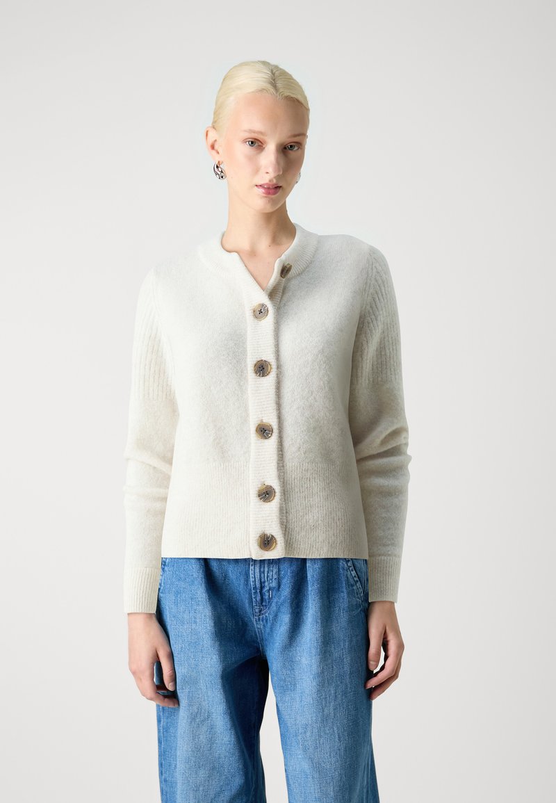 Cream-colored cardigan with a ribbed texture, featuring large wooden buttons, a rounded neckline, and long sleeves. Worn with blue jeans.