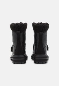 Botas negras hasta el tobillo que presentan una combinación de piel lisa y ante, un cuello de forro polar texturizado, suela gruesa con tacos y un detalle de hebilla en el lateral.