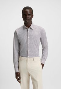 Camicia a maniche lunghe bianca con un piccolo motivo a pois neri, dotata di una chiusura con bottoni e colletto classico, abbinata a pantaloni beige chiaro.