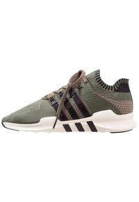 Gröna träningssneakers med en strukturerad ovandel, svarta ränder och vit sula. Funktioner inkluderar bruna snören och en mönstrad bakre krage.