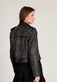 Giacca in pelle nera con decorazioni a borchie in motivi vorticosi, con taglio corto e ampi rever. Texture liscia, design moderno.