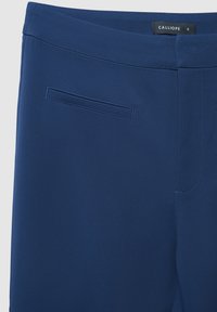 Pantalon bleu sur mesure en tissu texturé, avec une poche arrière et des coutures soignées. Étiquette indiquant "CALLIOPE", taille S.