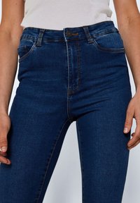 High-waisted blue denim jeans with a smooth texture, five-pocket design, and contrasting stitching on seams and pockets.