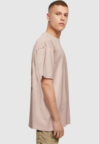 Light pink cotton t-shirt with short sleeves, relaxed fit, and graphic details on the side. Plain design, soft texture, and casual shape.