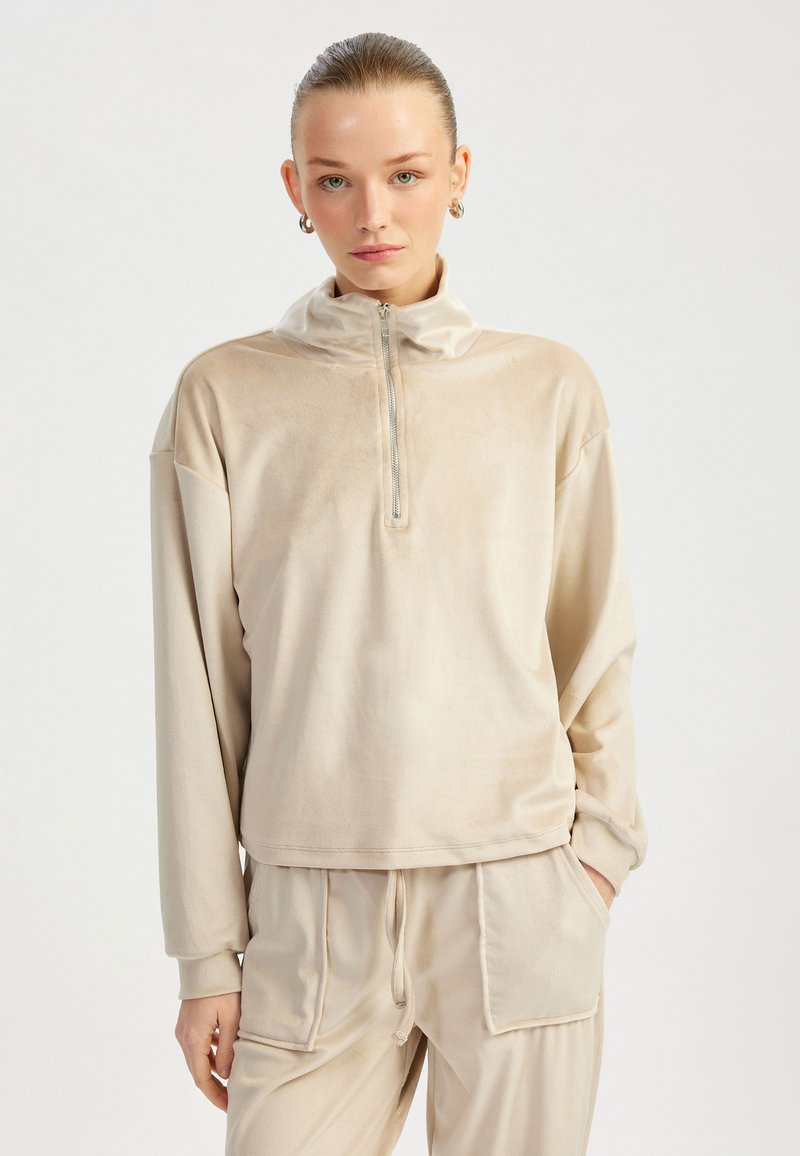 Beige, zip-hals pullover lavet af blødt materiale, med lange ærmer og en afslappet pasform, med en glat tekstur og minimalistisk design.