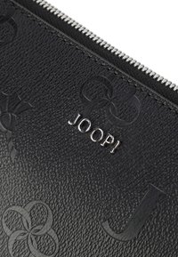 Čierna textúrovaná kožená taštička s embosovanými kvetinovými vzormi, striebornými kovovými prvkami a kovovým logom "JOOP!" na strede. Uzatváranie na zips.