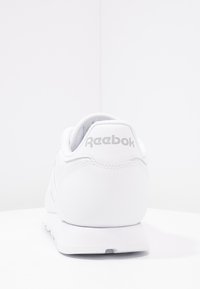 White Reebok sneaker with a smooth leather upper, round heel, and subtle branding on the back. Features a cushioned sole and stitched accents.