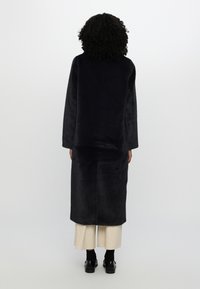 Long, dark navy fleece coat with loose fit and wide sleeves, reaching mid-calf. Paired with beige wide-leg pants and black shoes.