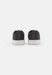 Zapatilla de lona negra con suela de goma blanca, con una textura suave y costuras traseras cosidas. Nombre de la marca "Levi's" grabado en el talón.