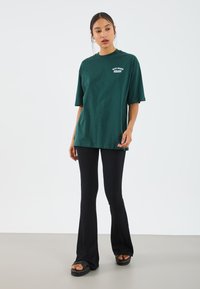 Green cotton t-shirt with a relaxed fit and short sleeves, paired with black ribbed flared pants and platform sandals with straps.