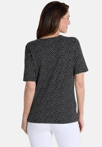 Zwarte korte mouwen shirt met een ronde halslijn, voorzien van een wit stippenpatroon. Glad materiaal met een relaxte pasvorm aan de achterkant.