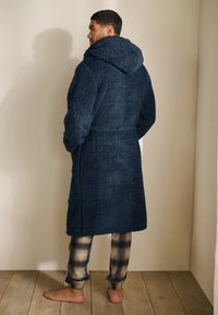 Marineblå fleecebadekåbe med hætte, med en tekstureret overflade, bælte ved taljen og længde til midt på læggen, kombineret med ternede pyjamasbukser.