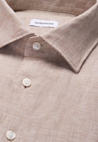 Chemise en lin beige avec col pointu, boutons blancs et étiquette de la marque "seidensticker" à l'intérieur du col.