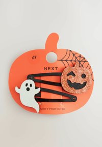 Dva crna češlja za kosu s blistavim ukrasima za Noć vještica: bijeli duh i narančasti jack-o'-lantern koji se smiješi, na narančastoj kartici u obliku bundeve.
