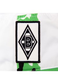 Witte stof met een groen en zwart camouflagepatroon. Heeft een zwart-wit, ruitvormig label met een gestileerde letter "B" in het midden.