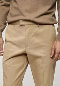 Pantaloni beige su misura realizzati in tessuto morbido, con frontale piatto, passanti per cintura e tasche laterali, dal taglio dritto.