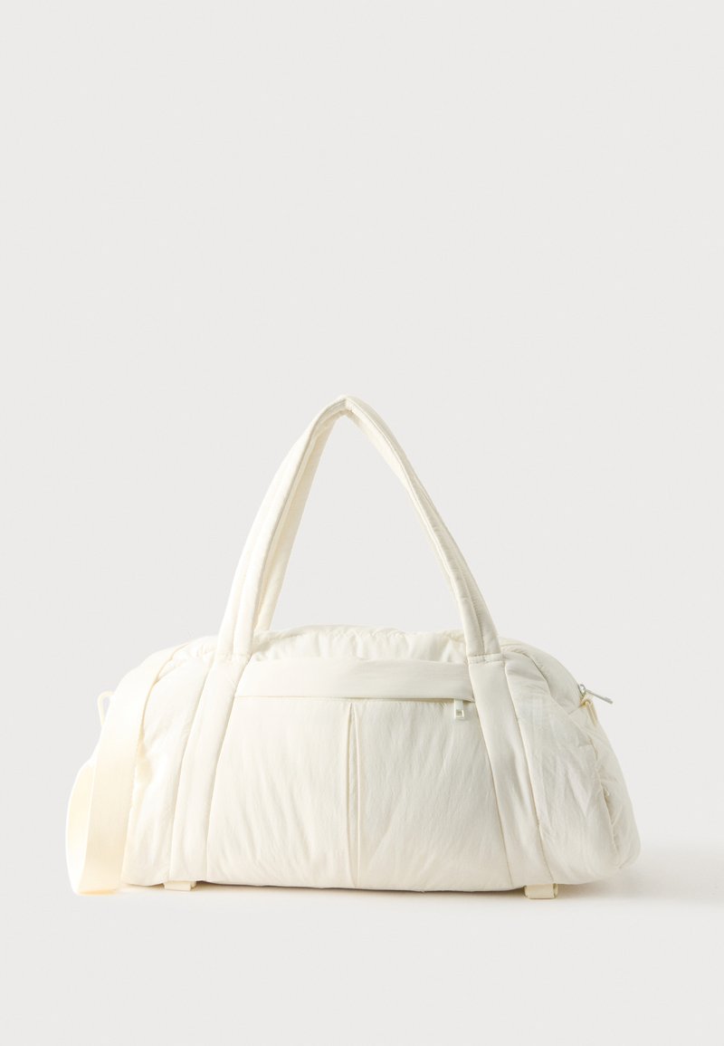 Sac polochon blanc doux avec deux poignées et une poche avant zippée, présenté sur un fond clair uni.