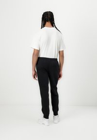 Schwarze Jogginghose mit elastischem Bund, kombiniert mit einem weißen kurzärmeligen Shirt. Das Outfit wird mit weißen Turnschuhen abgerundet.