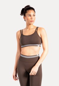 Sujetador deportivo marrón con tirantes ajustables y banda a rayas. Tejido liso y elástico con un diseño ajustado. Combinado con leggings de cintura alta a juego.