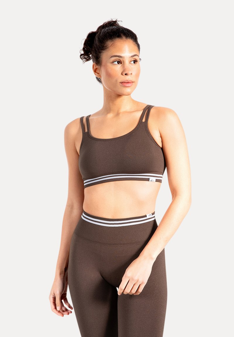 Sujetador deportivo marrón con tirantes ajustables y banda a rayas. Tejido liso y elástico con un diseño ajustado. Combinado con leggings de cintura alta a juego.