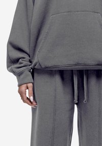 Grijze fleece hoodie met een voorzak, losse fit, geribde manchetten en een trekkoord in de taille op bijpassende joggingbroek. Zachte textuur, minimalistisch ontwerp.