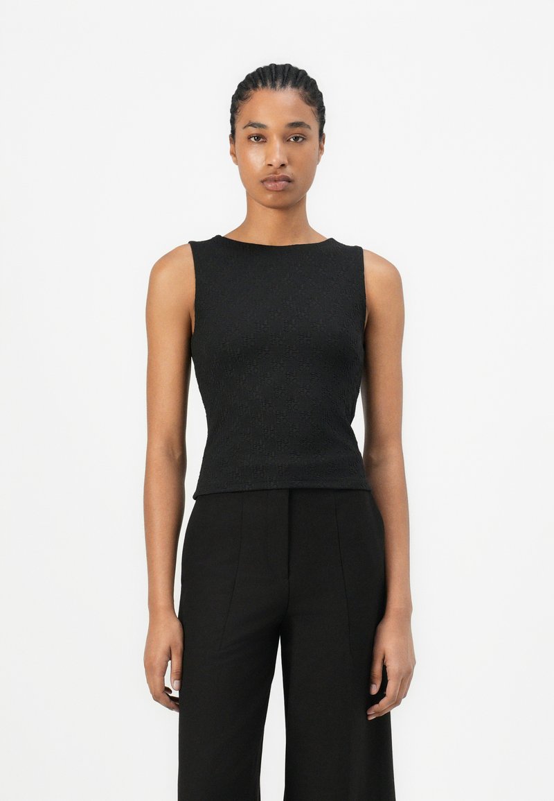 Zwarte, mouwloze top met een gestructureerd patroon, ronde halslijn en aansluitend ontwerp. Gestyled met zwarte broek met hoge taille.