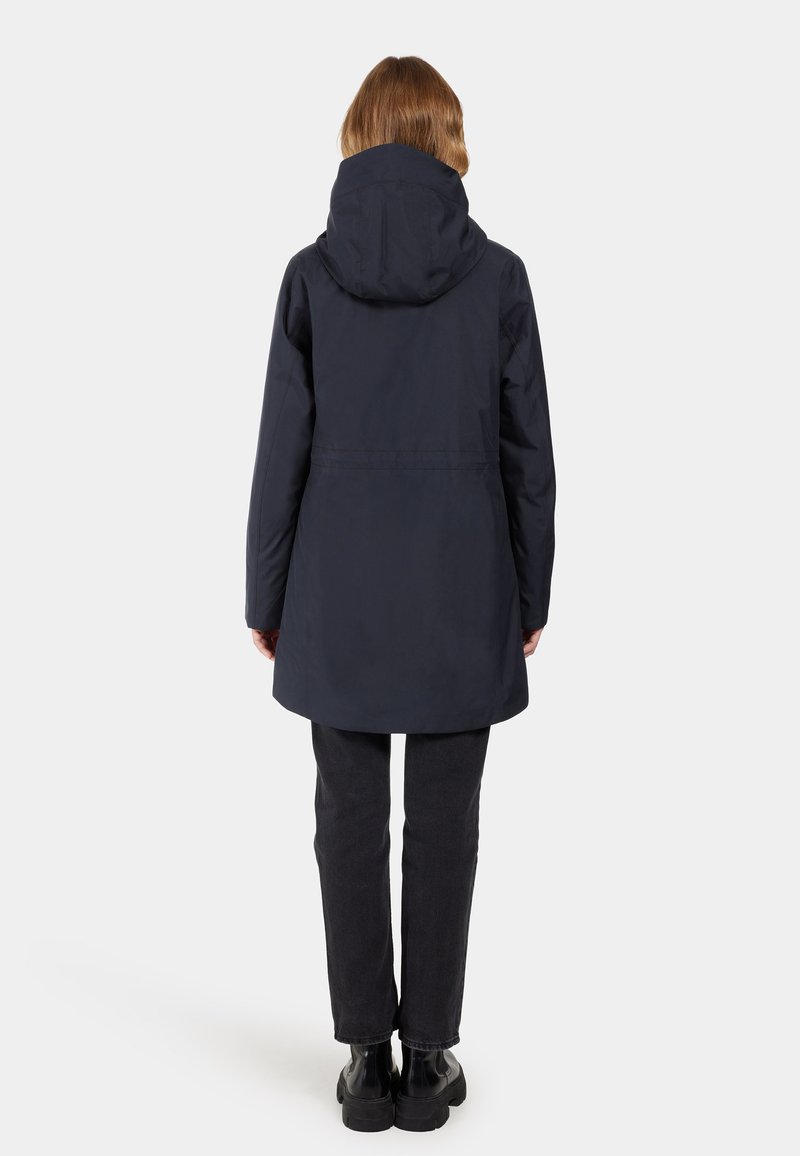 Marineblauer wasserdichter Mantel mit Kapuze; verfügt über einen geraden Schnitt, taillierte Taille und strukturiertes Material. Kombiniert mit dunkelblauen Jeans und klobigen Stiefeln.