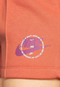 Gros plan d’un tissu orange avec le logo Nike violet et un texte circulaire blanc affichant la garantie de la marque et les marques déposées.