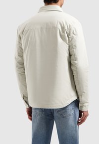 Lichtbeige colbert van lichtgewicht materiaal, met een gladde textuur en een relaxte pasvorm, gecombineerd met lichtblauwe jeans.