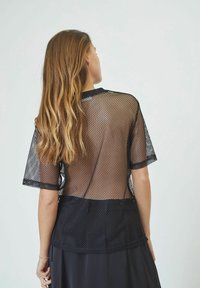 Top corto a maniche corte in rete nera con un design a rete testurizzato, dotato di un orlo nero solido. Il retro presenta uno stile semitrasparente.