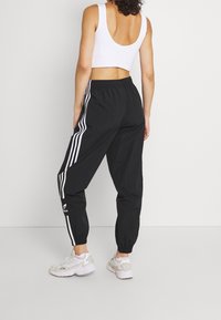 Svarta träningsbyxor med vita sidostreck och elastiska muddar. Matchat med en ärmlös vit crop top. Synlig logotypdetalj vid vristerna.