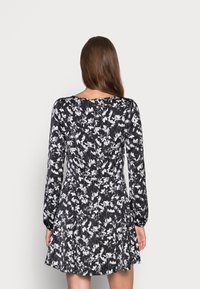 Långärmad klänning i svart tyg med vitt blommönster. Har en figursydd midja och utsvängd kjol. Bakifrån visar den en slät yta och rund halsringning.