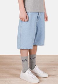 Ljusblå denimshorts med avslappnad passform, som sitter ovanför knäet, i kombination med grå strumpor med text och vita sneakers.