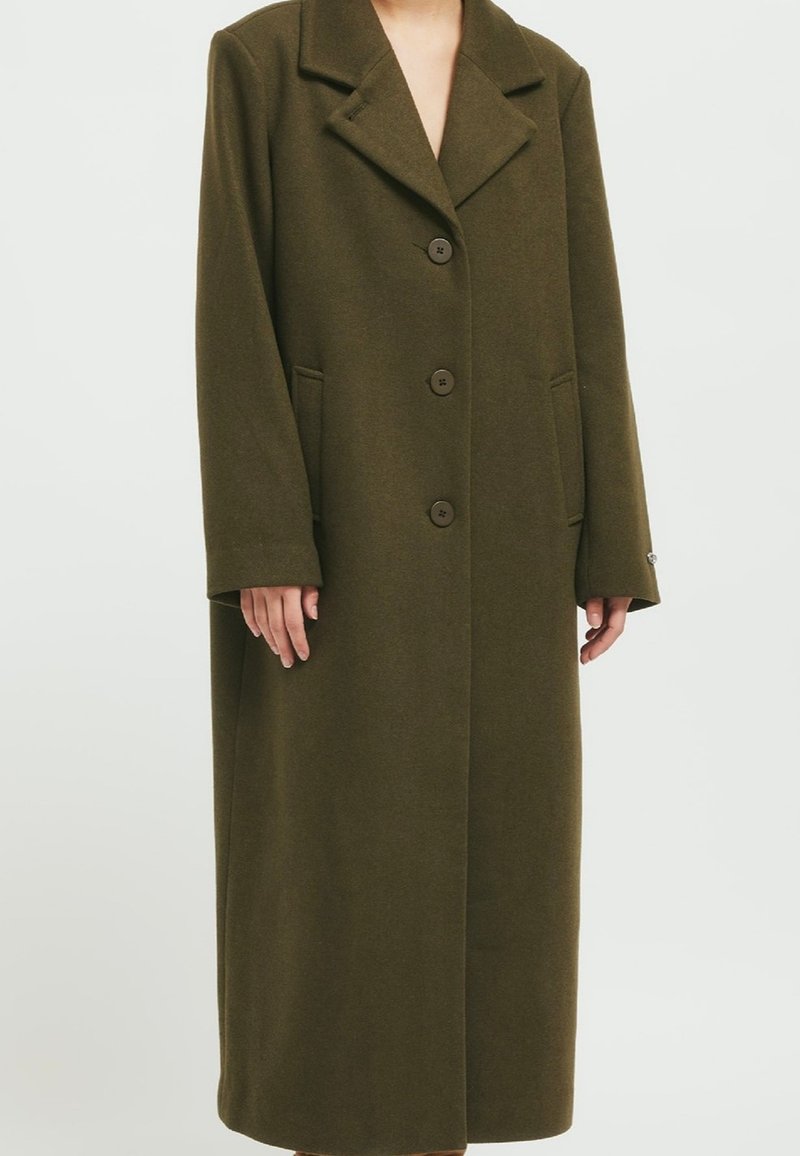 Olive green long wool coat with a notched collar, five buttons down the front, and side pockets. Features a straight cut and long sleeves.