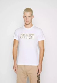 T-shirt bianco in cotone con stampa in foglia d'oro di "VERSACE JEANS COUTURE" sul davanti. Maniche corte, scollatura rotonda, vestibilità casual.