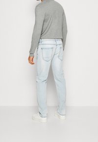 Jeans in denim blu chiaro con una vestibilità rilassata, cinque tasche e un lavaggio sbiadito. Abbinati a un top grigio a maniche lunghe e sneaker bianche.