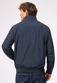 Giacca bomber blu navy con collo alto, polsini e orlo elastici. Tessuto liscio con dettagli di cucitura minimi, progettata per l'abbigliamento casual.