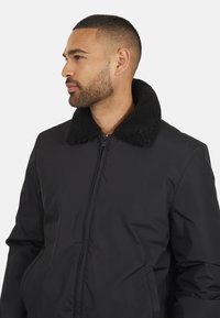 Giacca bomber nera con colletto in shearling nero testurizzato. Presenta una zip frontale, tasche laterali e un esterno in tessuto liscio.