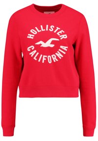 Sudadera roja de tejido suave con cuello redondo, puños acanalados y un estampado gráfico blanco que dice "HOLLISTER CALIFORNIA" junto a un diseño de un pájaro.