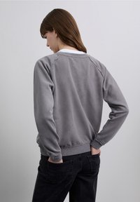 Gray sweatshirt with a soft texture, ribbed cuffs, and hem, featuring raglan sleeves. Worn with black jeans, showing a relaxed fit.