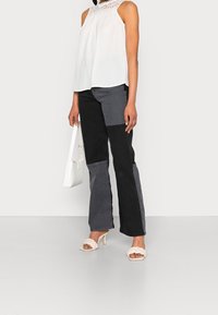 Vit ärmlös topp med spetsdetaljer; svart och grå lapptäckesbyxor med vida ben; vit handväska; nude klacksandaler med flätade remmar.