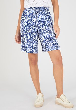 Femme portant un short bleu et blanc à imprimé floral longueur genou avec une taille élastique et des baskets blanches.