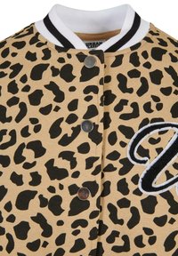 Jakna s uzorkom leoparda u bež i crnoj boji s ovratnikom na bijele i crne pruge, ima metalne dugmadi za pritisak i vezene detalje.