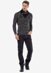 Schwarzer und grauer Strickpullover mit einem Schalkragen und Knopfdetails, kombiniert mit schwarzen Jeans und schwarzen Schnürstiefeln. Strukturmaterialien durchgehend.