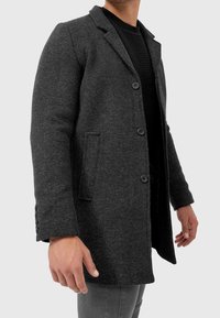 Grauer Fischgrätmantel, Wollmischung, einreihig mit zwei Vorderentaschen, Revers mit Schlitz, sichtbaren Knöpfen und strukturierter Stoff.