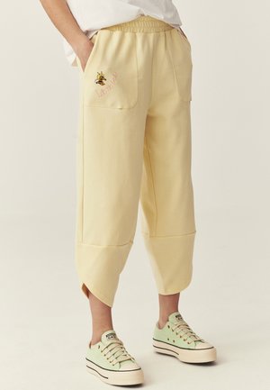 Luźne, jasnopółżółte krótkie spodnie z przodu z kieszeniami, haftem pszczoły oraz napisem "bądź wolny", noszone z jasnozielonymi sneakersami na platformie.