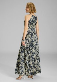 Kukkakuvioinen maxi-mekko tummansinisestä kankaasta, jossa on istuva yläosa ja virtaava hame. Hopeiset korkokengät ja käsikorut täydentävät asua.