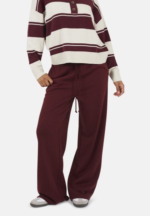 Pantaloni larghi color bordeaux con vita regolabile, abbinati a un maglione oversize a righe crema con tre bottoni marroni e polsini a coste.